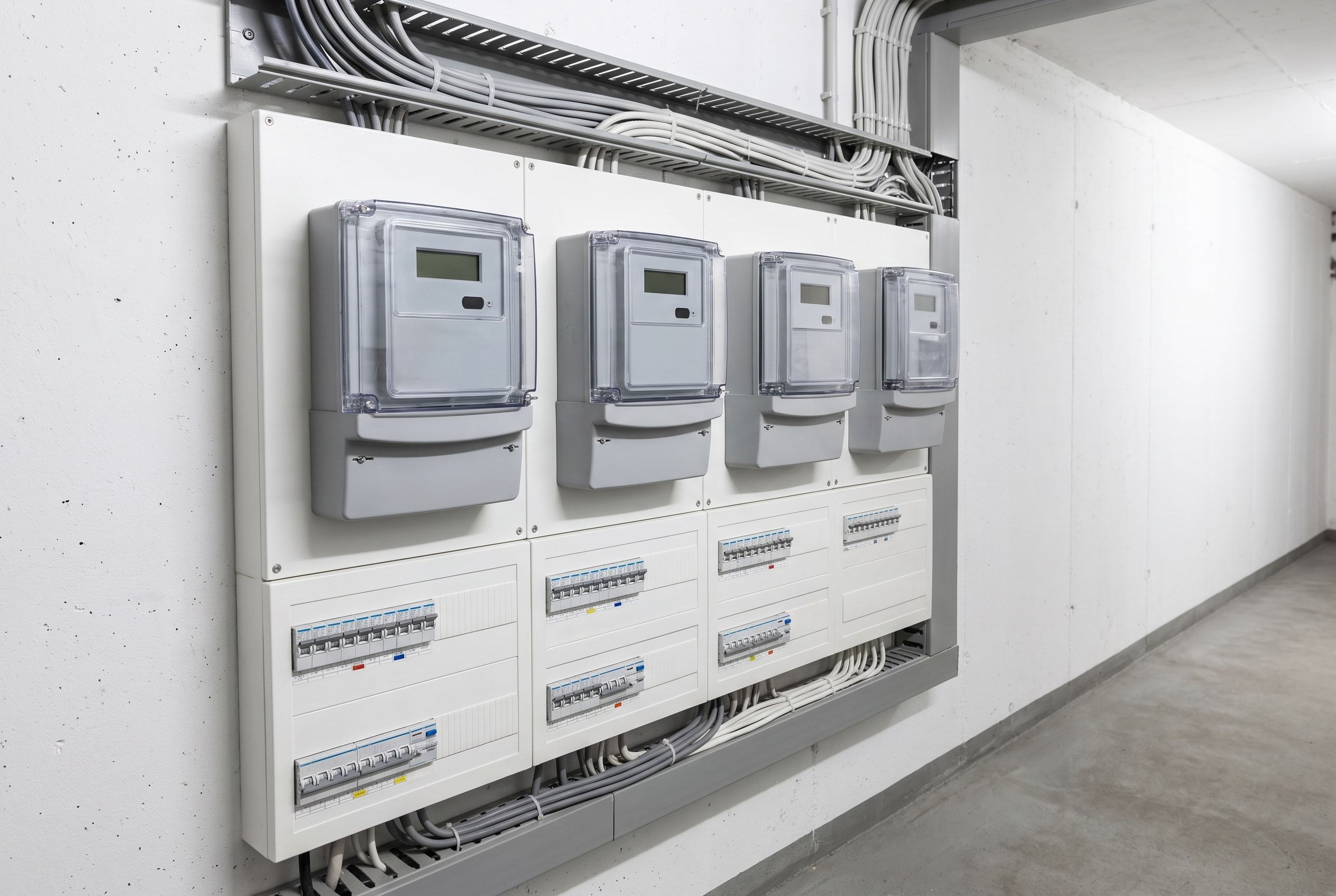 Tableau de comptage au sous-sol d’un immeuble : quatre compteurs électriques au-dessus des tableaux de distribution des logements